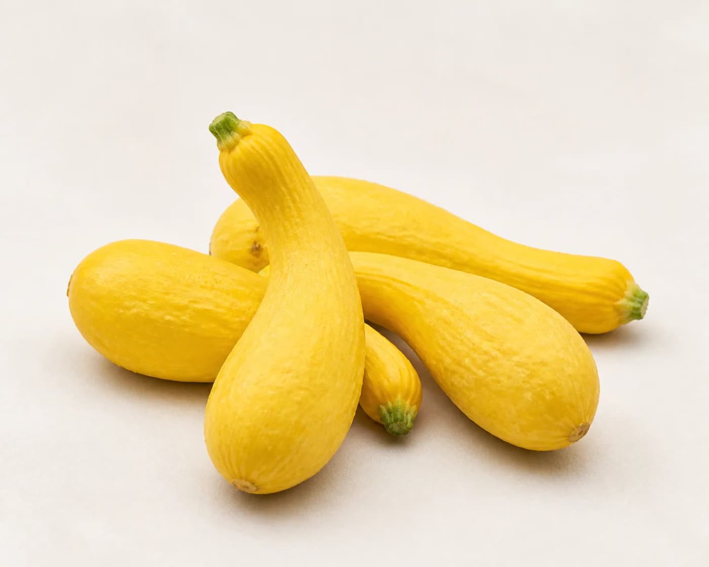 Fresh Yellow Crookneck Squash arranged on a warm off-white surface.