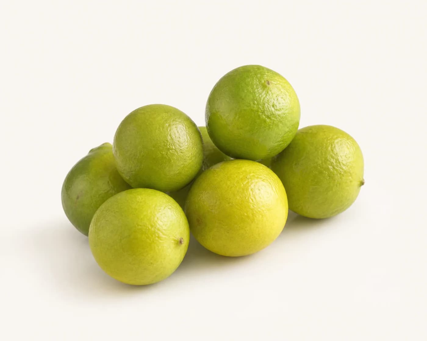 Fresh Kagzi Lime arranged on a warm off-white surface.