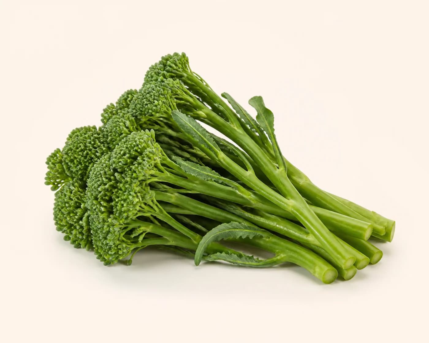 Fresh Broccolini arranged on a warm off-white surface.