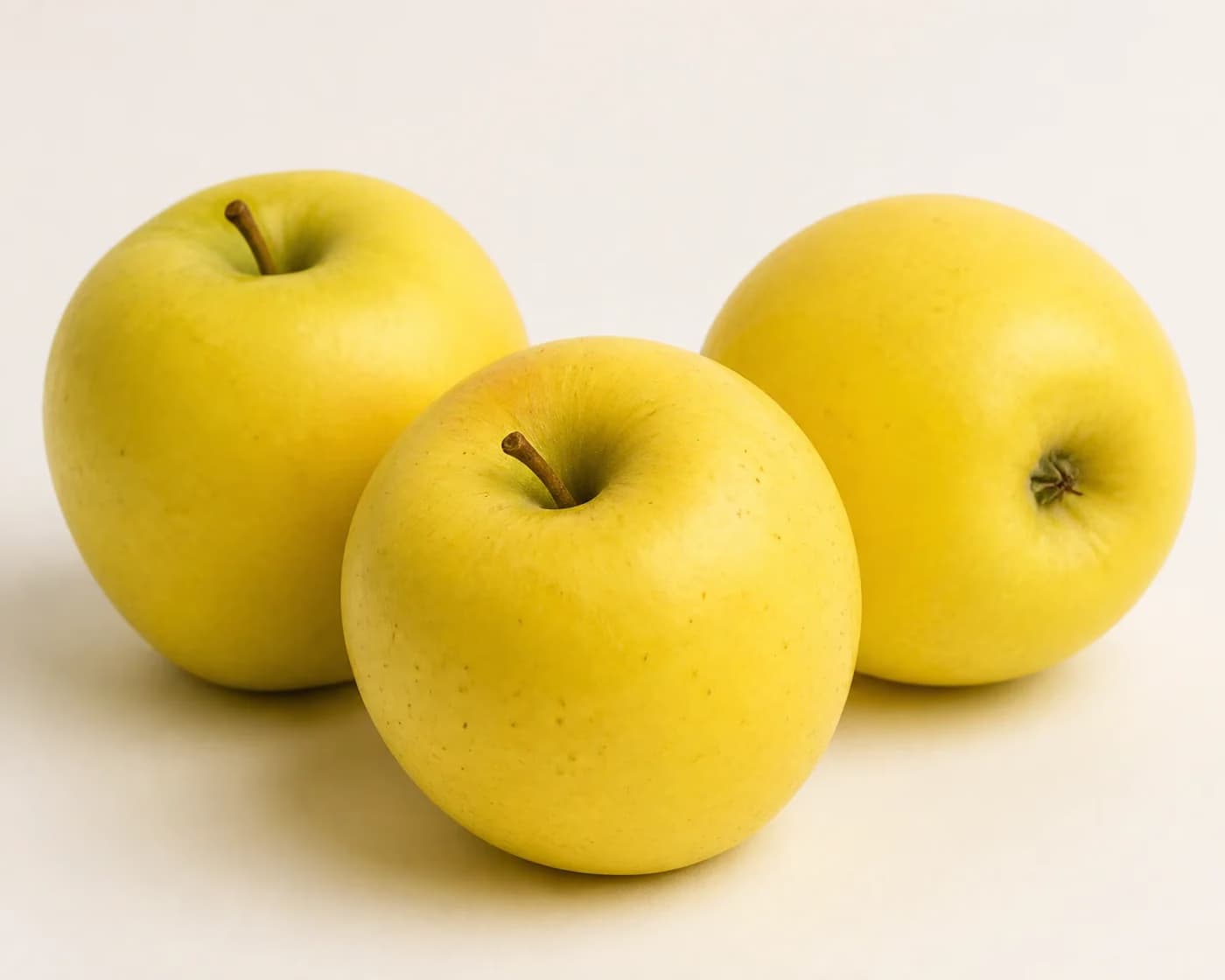 Fresh Golden Delicious Apple arranged on a warm off-white surface.