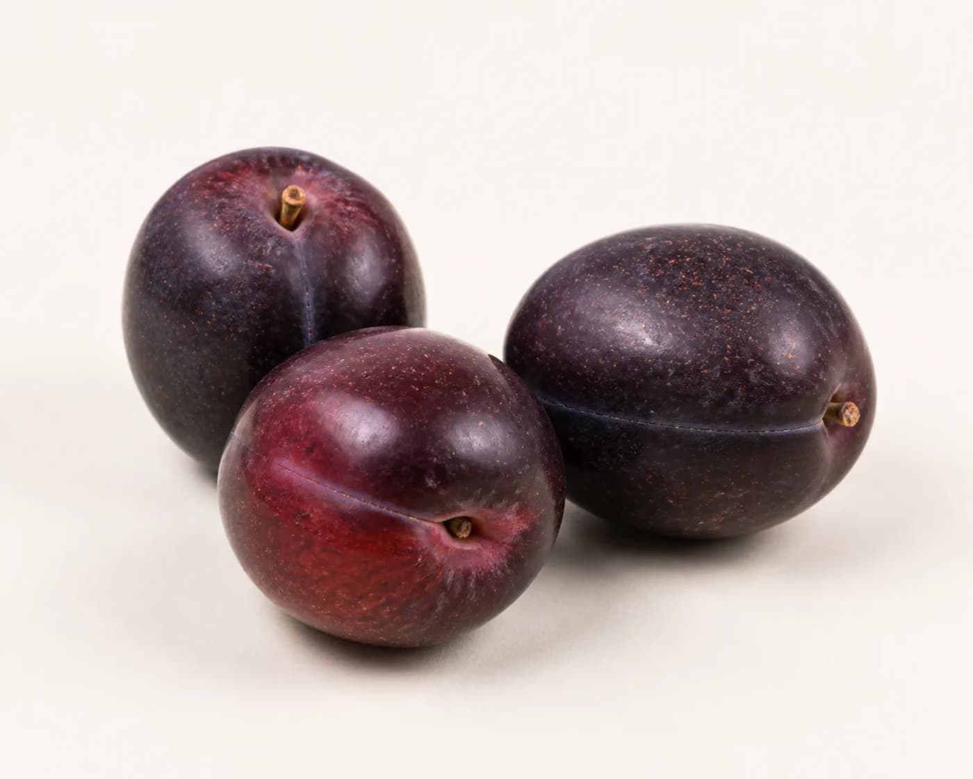 Fresh Black Amber Plum arranged on a warm off-white surface.