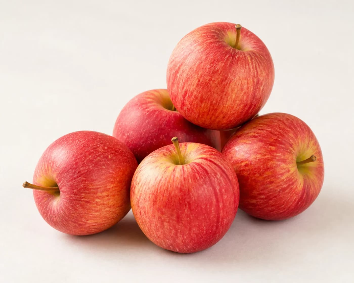 Fresh Royal Gala Apple arranged on a warm off-white surface.