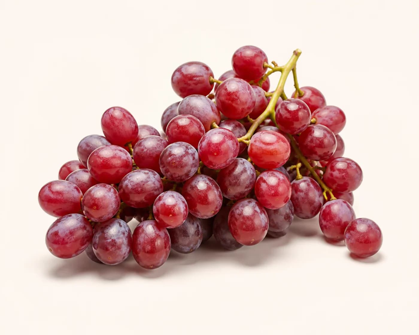 Fresh Red Globe Grapes arranged on a warm off-white surface.