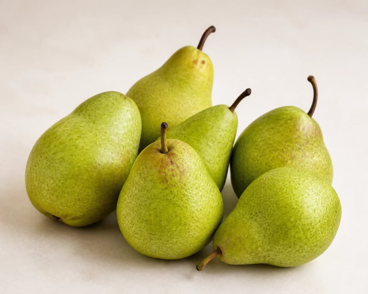 Fresh Green Pear arranged on a warm off-white surface.