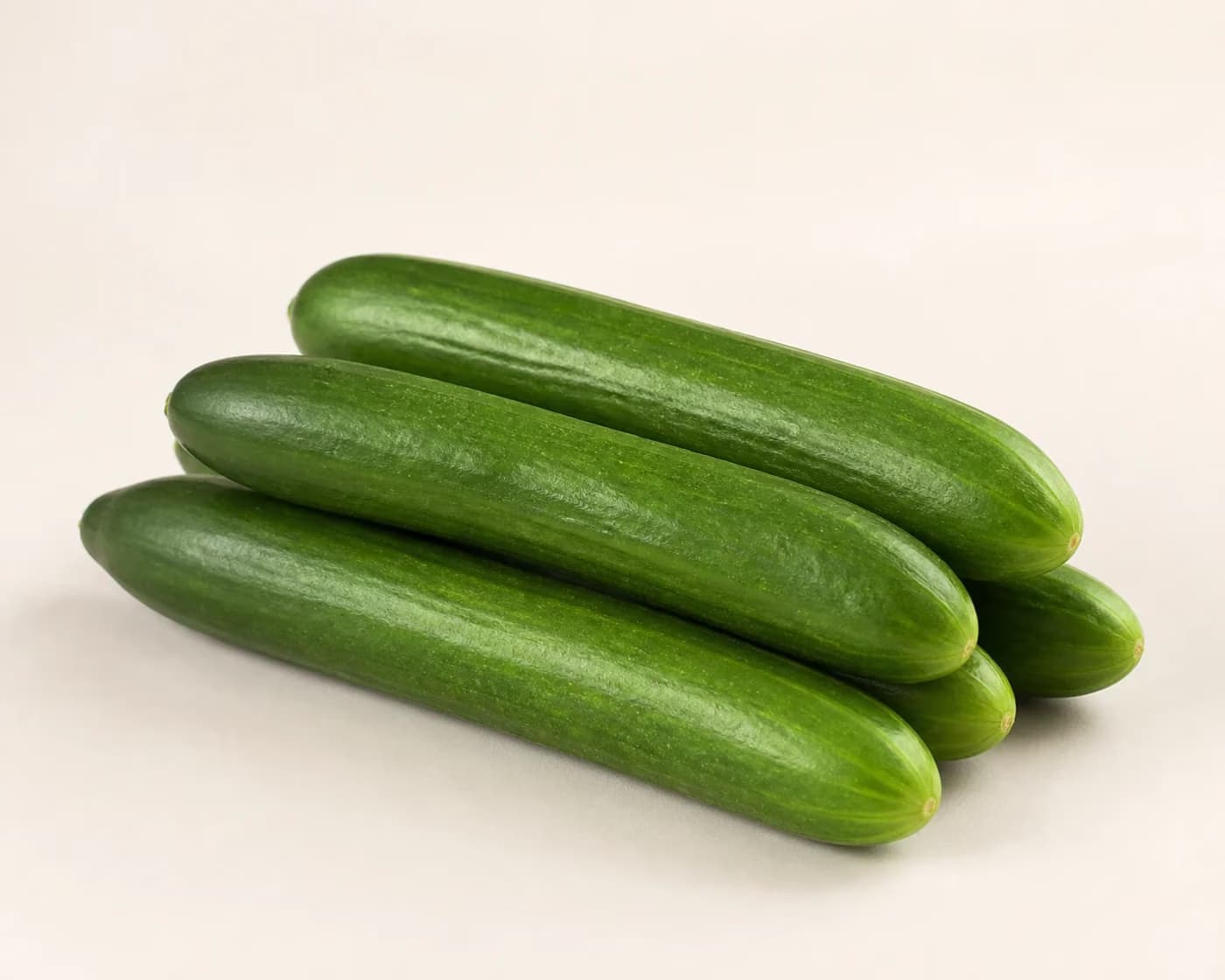 Fresh Hybrid Cucumber arranged on a warm off-white surface.