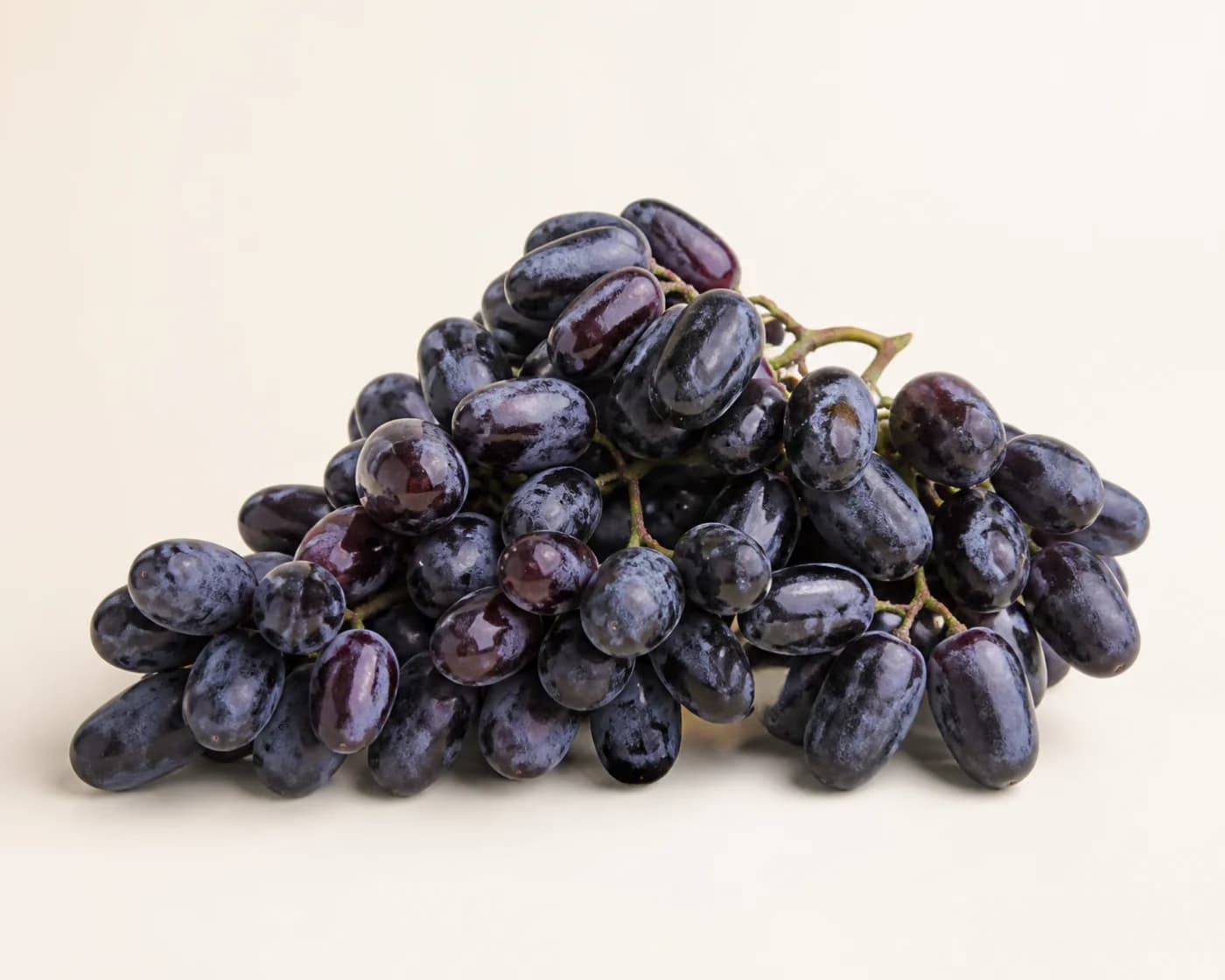 Fresh Bangalore Blue Grapes arranged on a warm off-white surface.