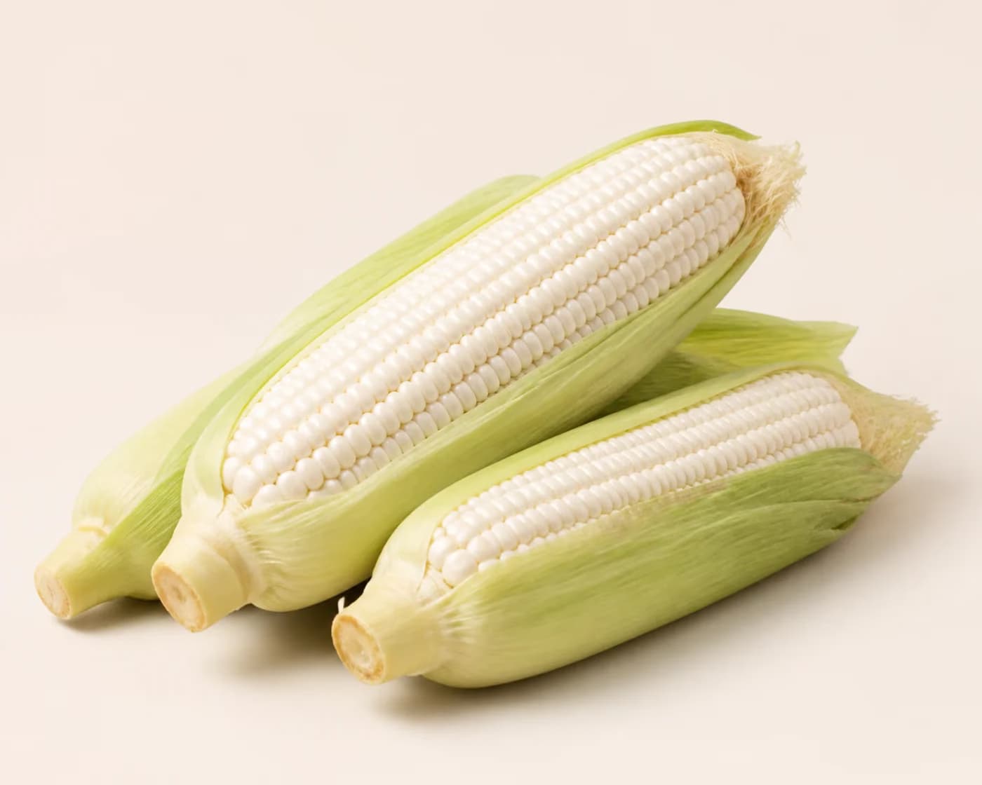 Fresh White Sweet Corn arranged on a warm off-white surface.