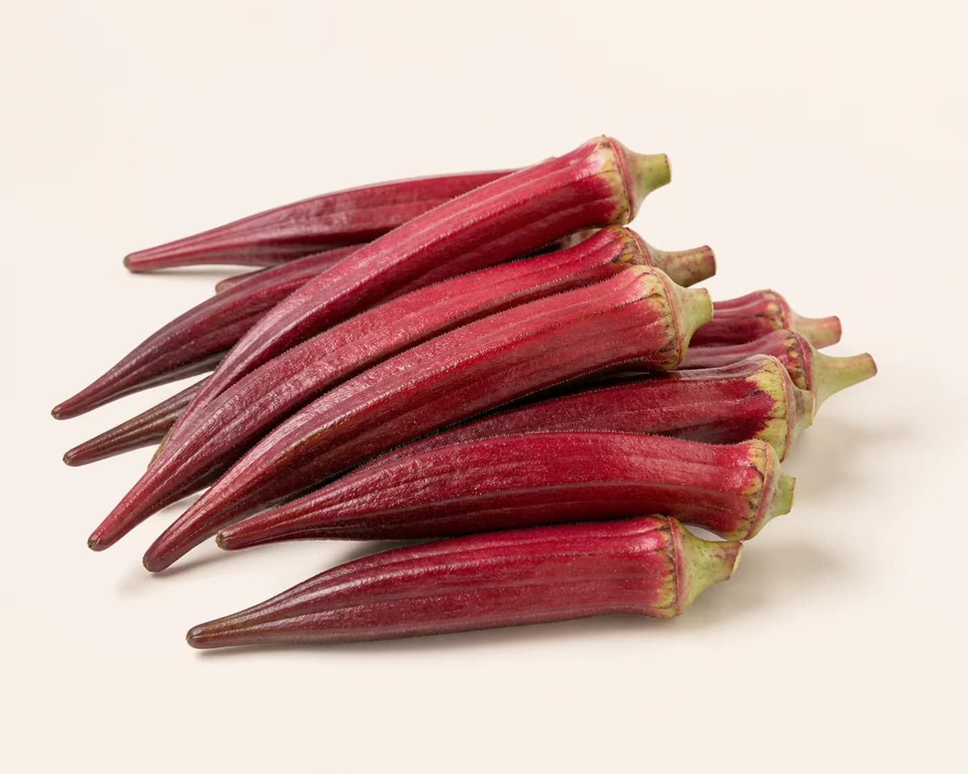 Fresh Red Okra arranged on a warm off-white surface.