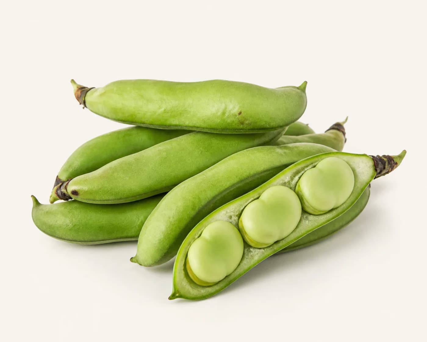 Fresh Broad Beans arranged on a warm off-white surface.