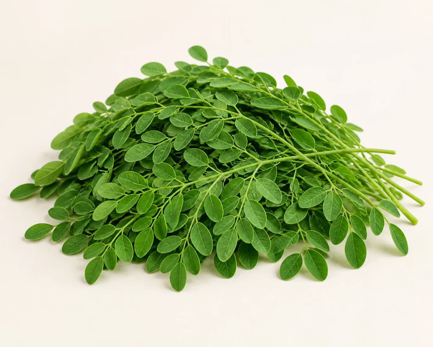 Fresh Moringa Leaves arranged on a warm off-white surface.