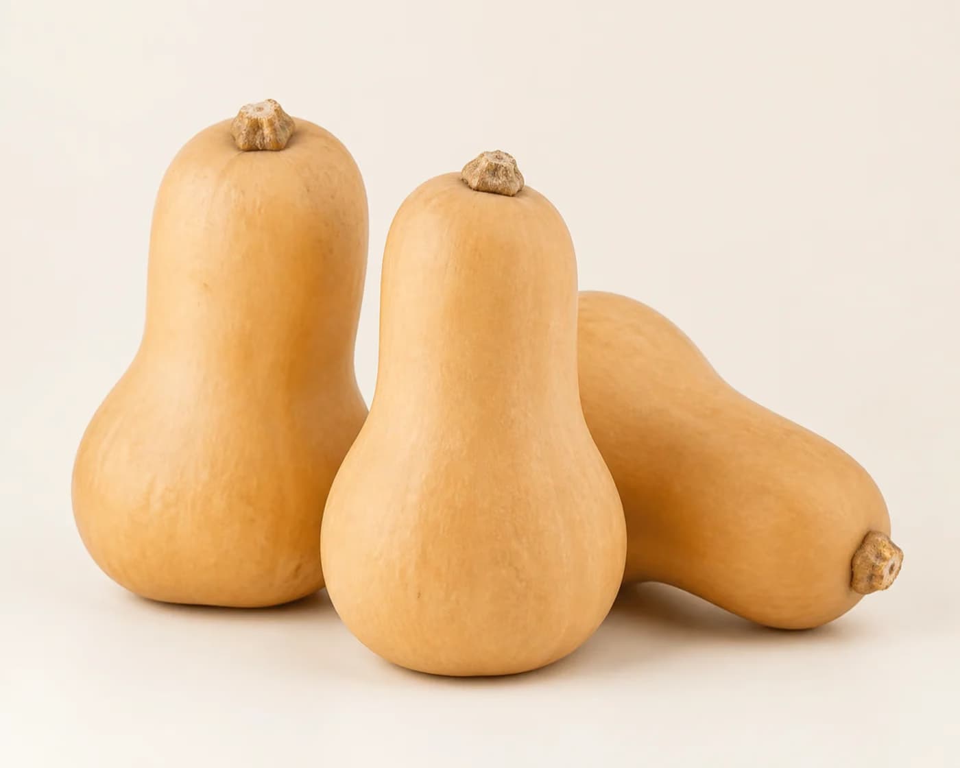 Fresh Butternut Squash arranged on a warm off-white surface.