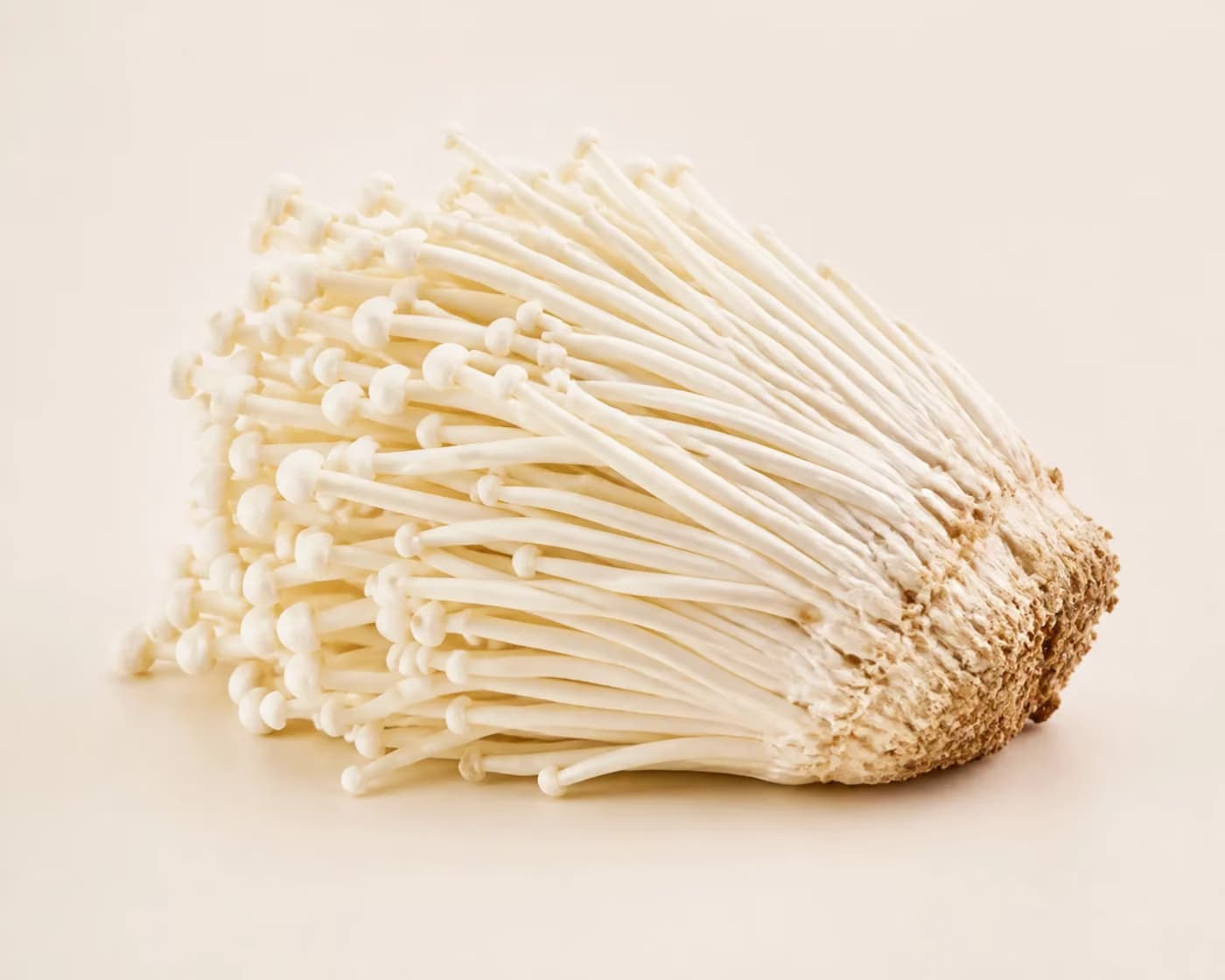 Fresh Enoki Mushroom arranged on a warm off-white surface.