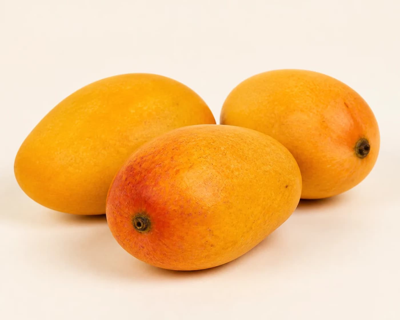 Fresh Kesar Mango arranged on a warm off-white surface.