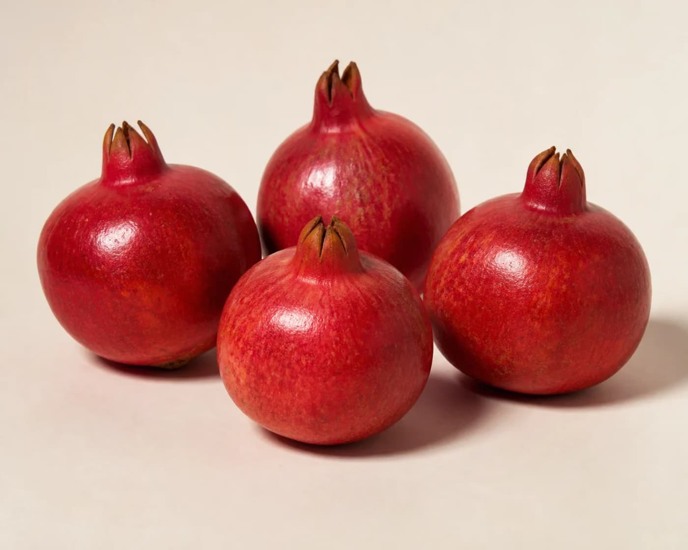Fresh Bhagwa Pomegranate arranged on a warm off-white surface.