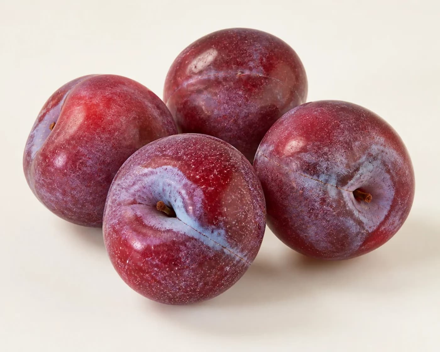 Fresh Santa Rosa Plum arranged on a warm off-white surface.
