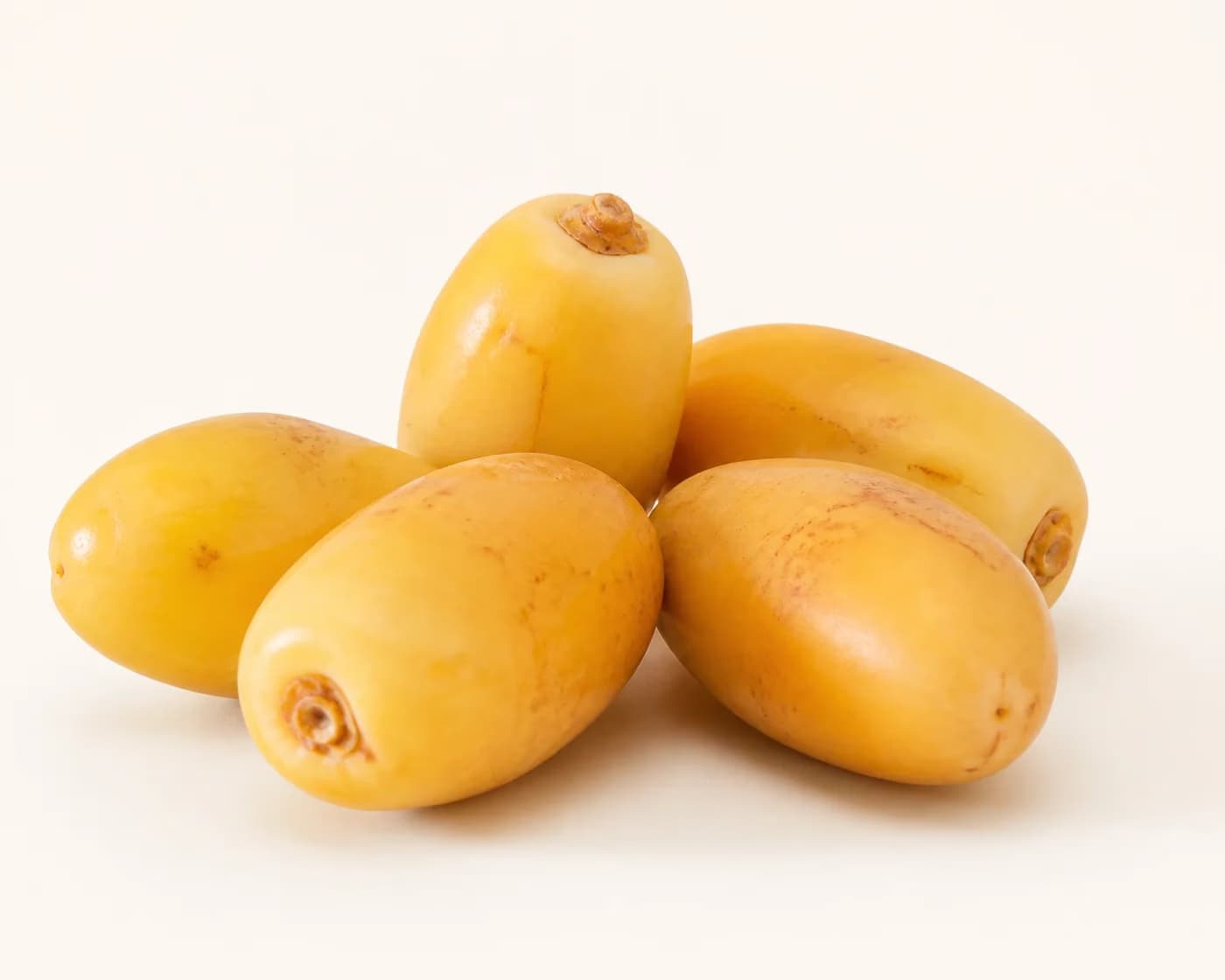 Fresh Fresh Yellow Dates arranged on a warm off-white surface.