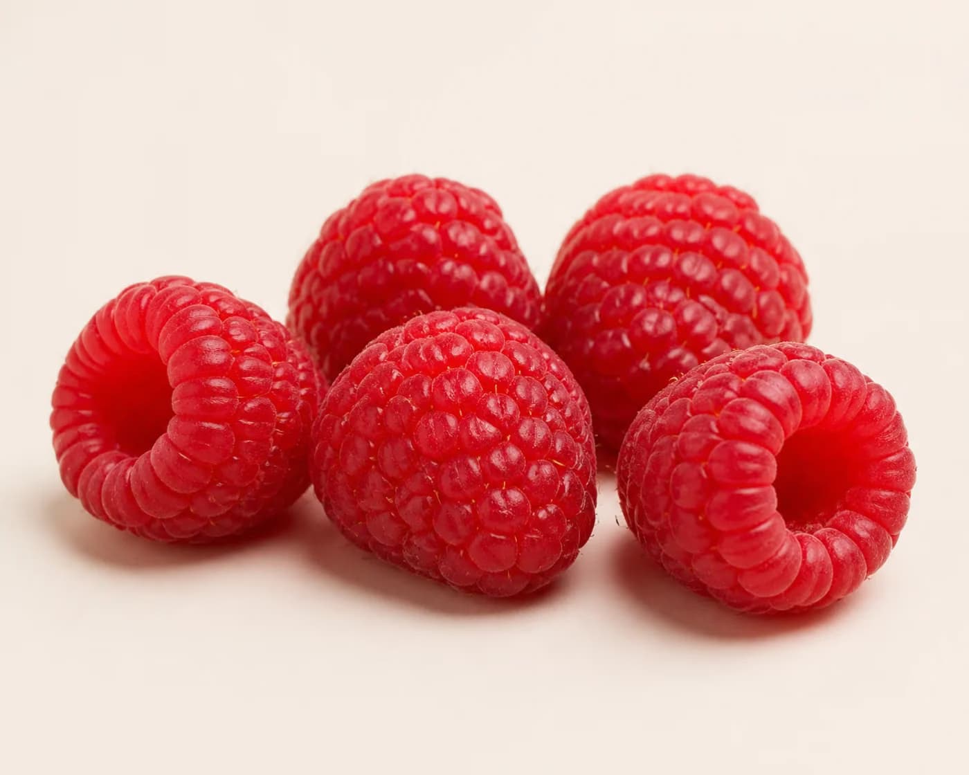 Fresh Raspberry arranged on a warm off-white surface.